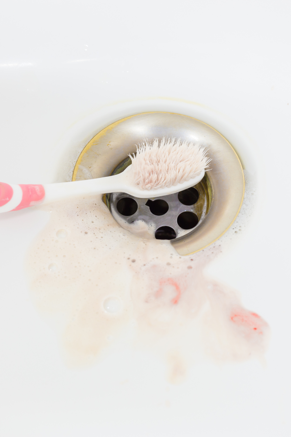 A toothbrush resting over a sink drain with pink-tinged foam, representing bleeding gums and PMOS | PCOS